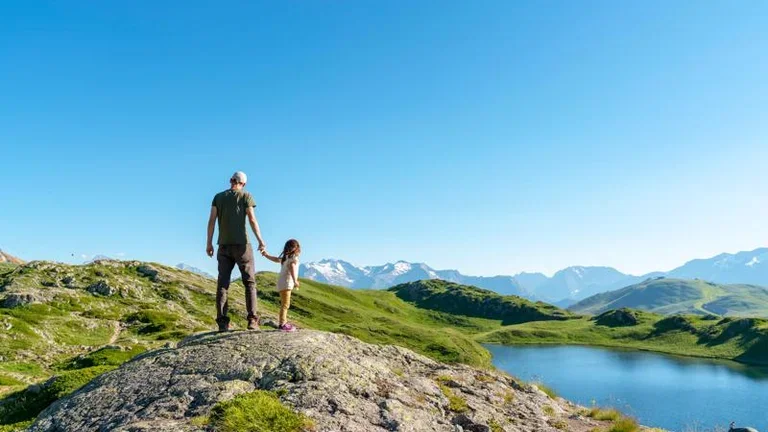 Father and daughter standing on rock object looking at view against clear sky